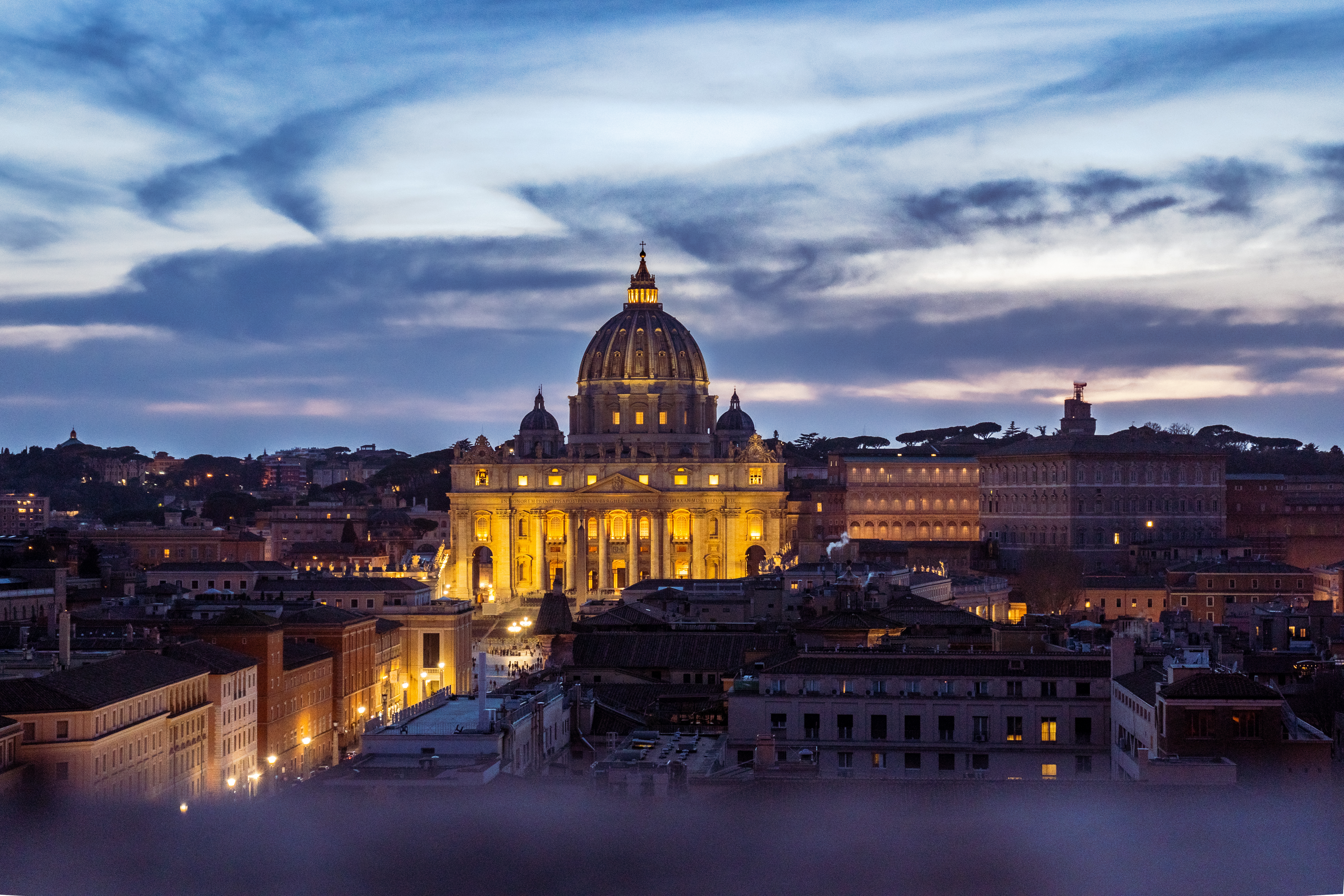 An elevated view of St. Peter's Basilica at dusk with the city skyline illuminated.