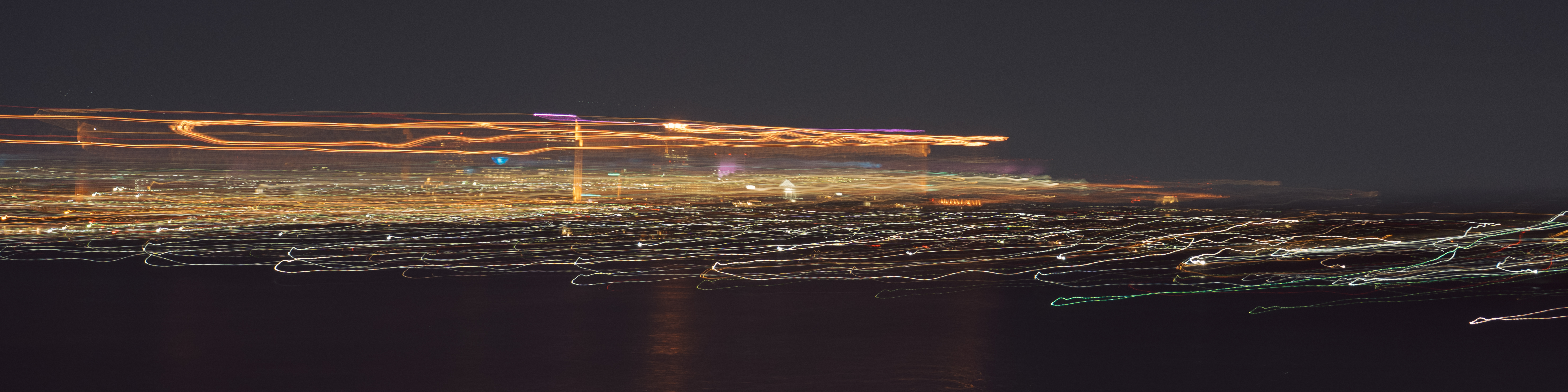 Panoramic long exposure of city lights streaking across a dark night sky.